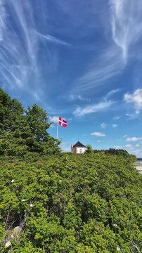 Vertical video of the historic yellow tea house at Castle on Tasinge island near Svendborg with the national Dannebrog flag waving under a beautiful sky.