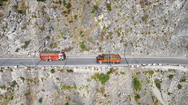 Drone shot of commercial lorries navigating a steep cliff road in India.