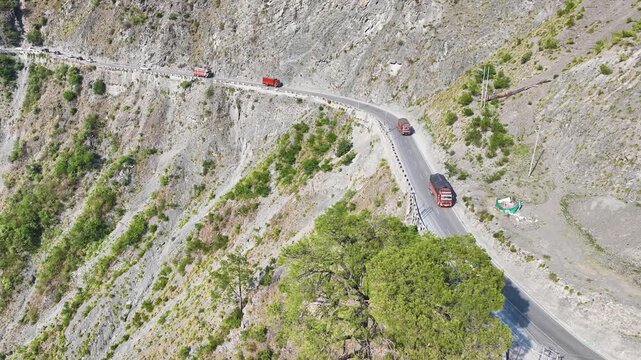 Aerial view of cargo trucks driving on dangerous Himalayan mountain road.