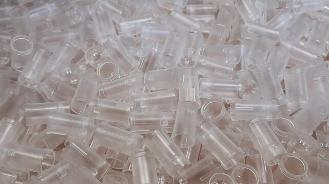 ): Industrial video of clear transparent plastic components piled up. Abstract factory background of manufactured polymer details, medicine or engineering synthetic items.