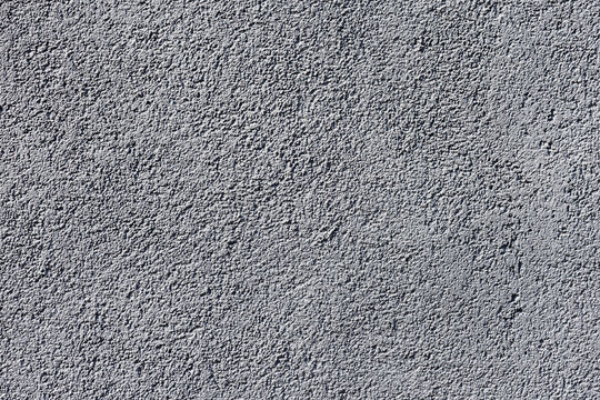 A factual close-up of a rough grey stucco wall, showcasing a coarse granular texture and neutral lighting, ideal for minimalist backgrounds and graphic design projects.