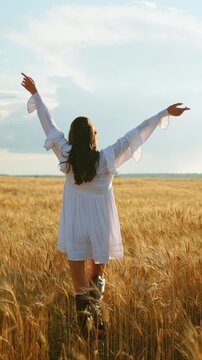 Woman in white dress moving through golden wheat field from open arms to quiet pause