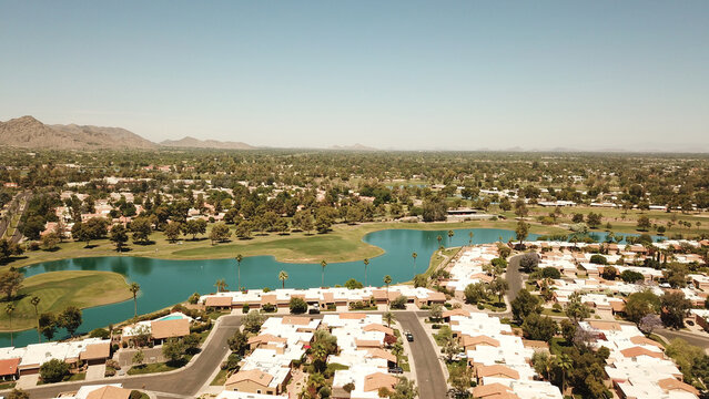 Aerial view of a residential neighborhood with a winding lake and golf course, surrounded by desert landscape and distant mountains in Phoenix, Arizona, United States.