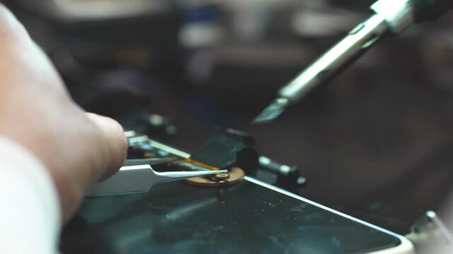 Close-up of technician repairing laptop video connector with precision soldering tools