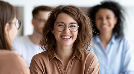 Obraz premium Happy young woman smiling in casual outfit with blurred coworkers in office