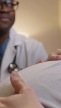 Vertical video: Leaning clinician palpating pregnant belly in clinic with stethoscope for checkup