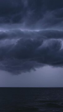 Vertical video: Glowing shelf cloud responding to forked lightning striking left horizon over ocean