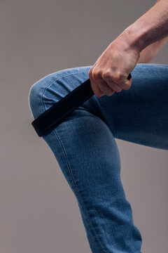 A muscular man in blue classic jeans with a bare torso is holding a belt. Concept: domination and play in a married couple, domestic violence, getting ready for work in the morning