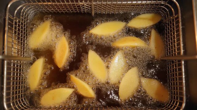 Frying potato wedges, golden brown in deep fryer basket, sizzling hot oil, bubbling and frying, symbolizing cooking, food preparation, and culinary arts