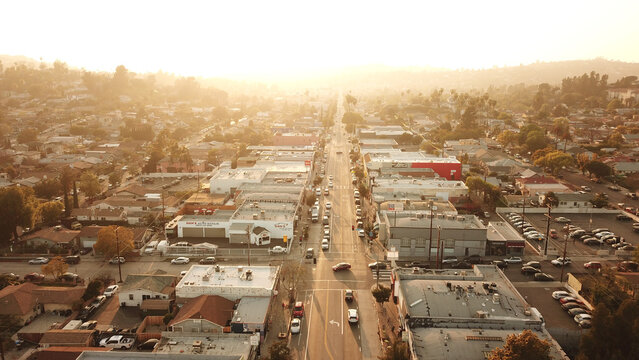 Aerial view of Highland Park in Los Angeles, California, United States, featuring a long street lined with commercial buildings and residential rooftops bathed in warm golden hour light.