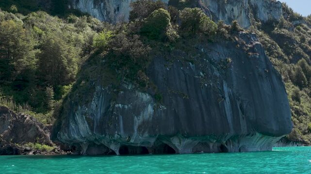 Exterior view of the massive Marble Chapel rock formation, featuring water-eroded textures and lush forest vegetation, situated on the shores of General Carrera Lake, Patagonia, Chile.