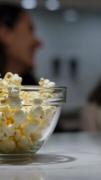 Vertical video: Showing glass bowl popcorn at kitchen counter as 2 women socializing in muted tops