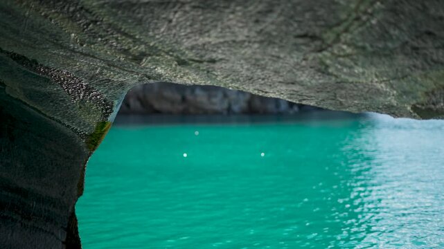Close-up view from inside a natural marble cave, focusing on the textured rock ceiling and bright sunlight bokeh reflections on the vibrant turquoise water.