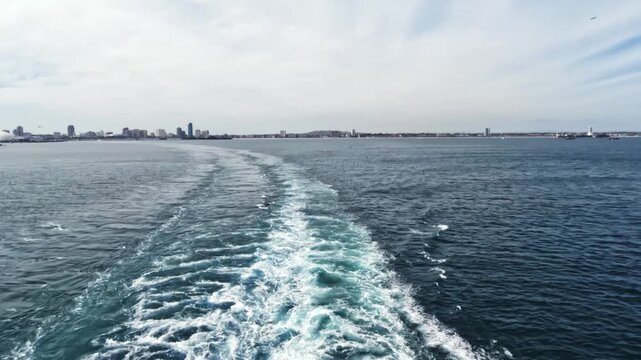 Scenic footage of a cruise ship sailing away across the open ocean, leaving behind visible ship tracks on the water surface.
