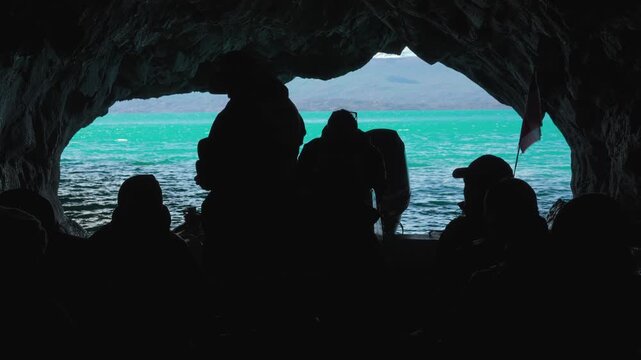Silhouetted group of tourists in a boat looking out from inside the Marble Caves towards the turquoise waters of General Carrera Lake, Patagonia, Chile.