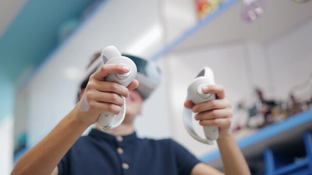 Portrait happy Boy wearing virtual reality headset interacting with controllers indoors.