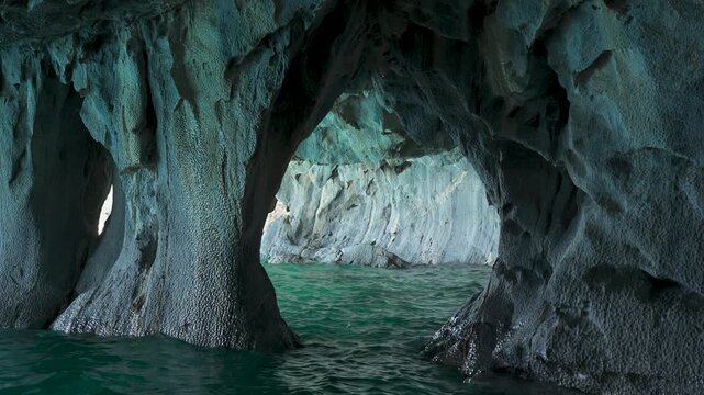 Interior view of natural marble cave formations with stone walls sculpted by water and deep turquoise water, wide shot of a wild and exotic geological environment.