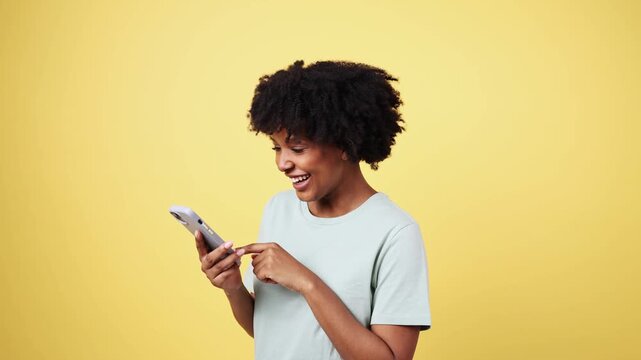 Happy african american woman using smartphone on yellow background
