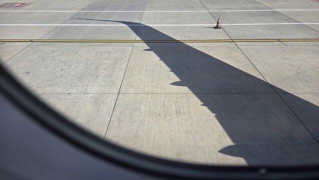 Airplane wing shadow on airport tarmac framed by cabin window for travel background and industrial poster design