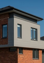 Obraz premium Contemporary suburban house exterior featuring mixed cladding of dark red brick and smooth gray stucco, showcasing clean lines and large windows, geometric, house, dwelling