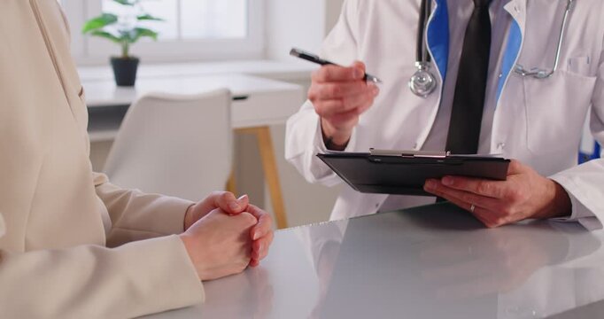 Male doctor talking with female patient sitting on workplace at desk in clinic. Physician giving consultation a woman during medical examination in office. Medicine concept. 4k video.