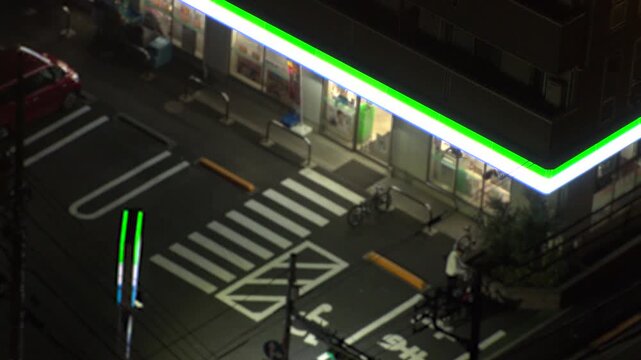 TOKYO, JAPAN - JUNE 2026 : Aerial view of convenience store at night. Glowing neon lighted konbini shop entrance on urban street. Japanese nightlife and urban lifestyle concept video. Time lapse shot.