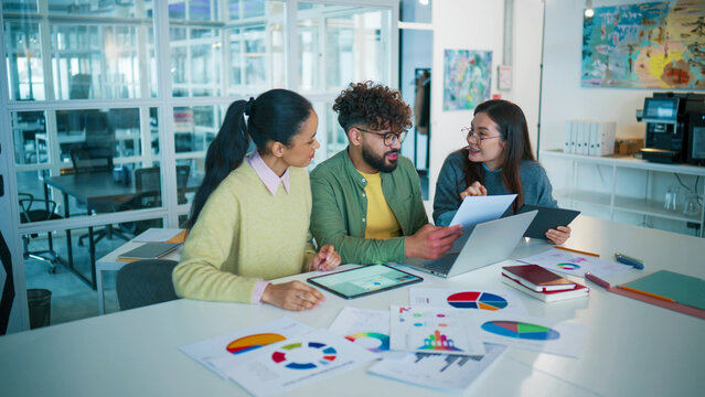 Dynamic view of startup team celebrating success. Male giving high five to female colleague. Woman raising hand with excitement. Holding tablet and laptop on desk. Achieving business goals.