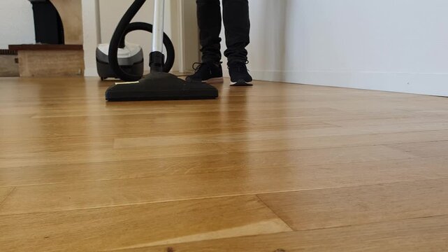 Young man vacuuming hardwood floor with low angle close up view