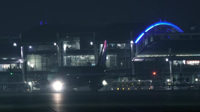 Passenger Airplane Taxiing from Terminal Gate to Runway at Night | Airport Illuminated with Blue Lights |  Telephoto Aviation Scene