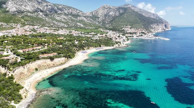 Aerial 4K footage of the crystal-clear turquoise sea off Cala Gonone, Sardinia, on a sunny summer day. Calm Mediterranean waters, blue sky, and pristine coastline create a stunning natural seascape