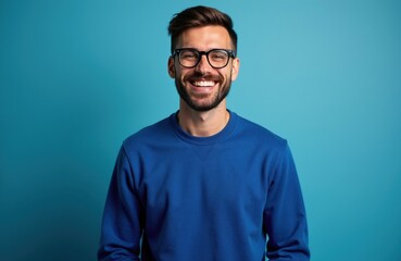 Fototapeta premium Smiling man wears glasses, blue sweater against solid background. Attractive male with beard shows joy radiates positivity. Portrait conveys confidence success friendly vibe ideal for business