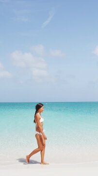 Vacation Travel Beach Life. Woman in bikini walking on paradise beach with white sand turquoise water. Beautiful multiracial Wasian model in summer. Video is unretouched and model without makeup.