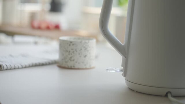 Hand places electric kettle on base and presses power switch on kitchen counter. Concept of boiling water and tea preparation