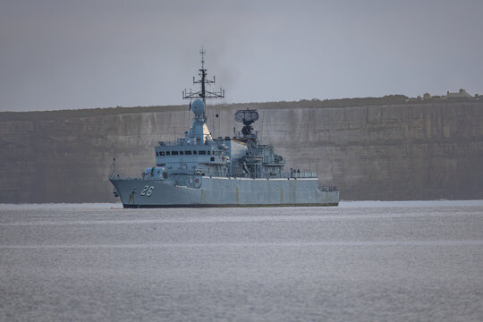 A 40 year old Royal Malaysian Navy corvette warship anchored in calm waters in front of huge vertical sandstone cliffs, in a co-operative outing with the Australian navy at Jervis Bay in Australia. 