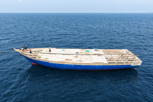 Aerial view of a large wooden boat under construction floating in the deep blue ocean with workers on the deck in Vaikaradhoo, Haa Dhaalu Atoll, Maldives.