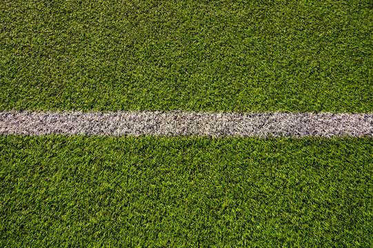 Top view of artificial green grass with white marking line on soccer field. Synthetic sports turf texture background. Football pitch lawn pattern