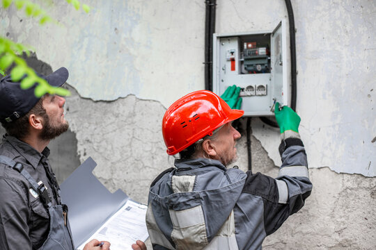 Technical specialists reviewing documentation while inspecting an open electrical panel. utility audit, power network maintenance, industrial supervision.