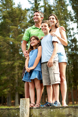 Naklejka premium Holiday, lake and happy family with children in nature for outdoor bonding, weekend or getaway. Mom, dad and kids with smile on lakeside bridge for sightseeing adventure, travel or vacation together