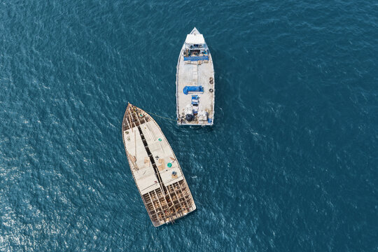 Aerial view of two boats floating in the deep blue sea, one traditional wooden dhoni under construction and one smaller utility vessel, in Vaikaradhoo, Haa Dhaalu Atoll, Maldives.