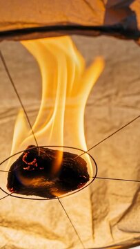 Vertical video: Burning fuel tablet flickering since ignition, hanging inside paper shell on wires