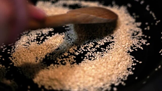 Stirring sesame seeds on a hot pan for sushi, close-up.