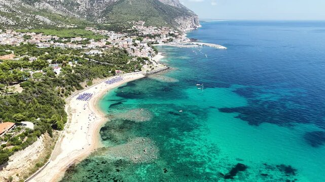 Aerial 4K footage of the crystal-clear turquoise sea off Cala Gonone, Sardinia, on a sunny summer day. Calm Mediterranean waters, blue sky, and pristine coastline create a stunning natural seascape