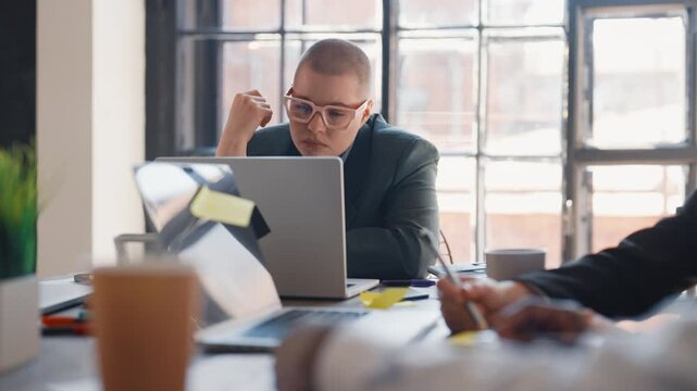 Young adult woman is bored in office coworking space, portrait in working day. Smart female professional thinking about project, looking at laptop display, troubles in job, hard career perspective