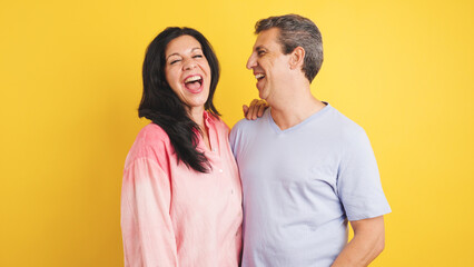 Naklejka premium Cheerful adult man and woman sharing a moment of genuine laughter and joy, embracing partnership and togetherness on yellow background