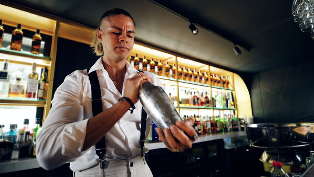 Professional bartender preparing a cocktail with a shaker, mixing ingredients for a beverage at a modern bar counter