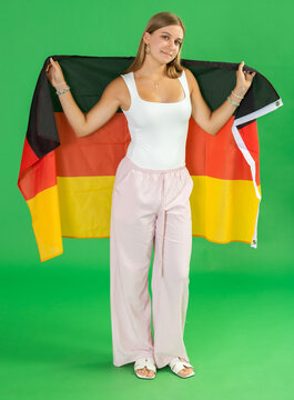 Teenage girl stands against green screen, holding large German flag