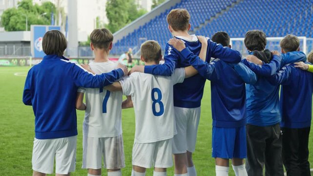 Football team players stand and hug while waiting for a penalty kick in their goal and rejoice after the opponent misses, view from behind