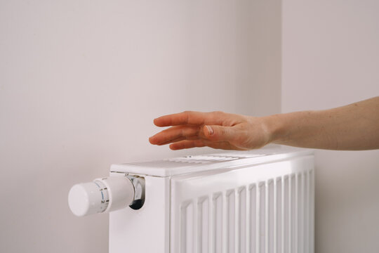 Hand checks warmth of home heating radiator in modern apartment