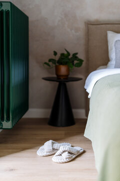 Warm radiator in cozy bedroom next to bed and plant on nightstand
