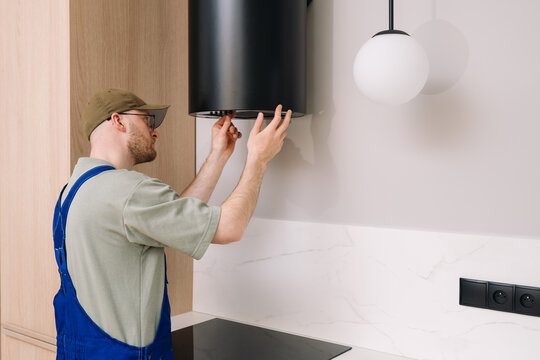 Man technician installing kitchen hood in modern apartment